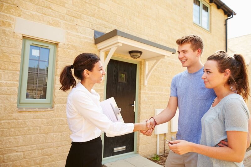 A real estate agent shaking hands with clients outside a house.